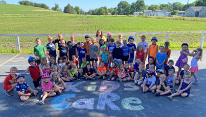 Children gather around a sidewalk chalk sign that says "Kids Care".