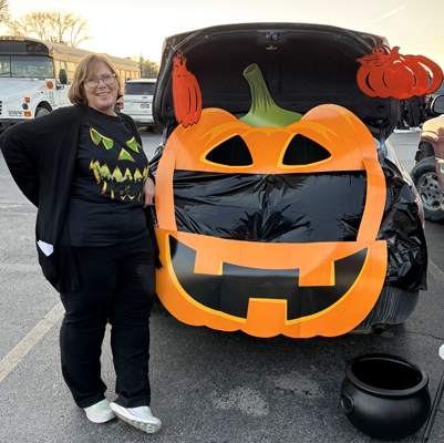 Generous woman with candy in front of jack-o-lantern trunk